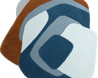 Puede incluir: Alfombra abstracta con un esquema de color azul, marrón y blanco. La alfombra tiene una forma única y orgánica y está hecha de un material suave y mullido.