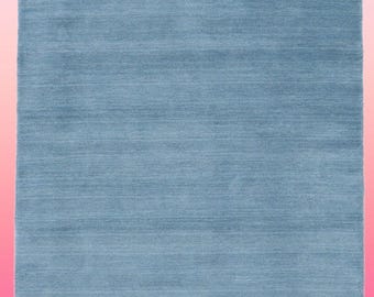 May include: A solid blue rug with a fringed edge. The rug has a subtle texture and a slightly faded appearance.