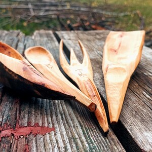 K&ouml;nnte beinhalten: Ein Set aus vier handgeschnitzten K&uuml;chenutensilien aus Holz: ein gro&szlig;er L&ouml;ffel, ein kleiner L&ouml;ffel, eine Gabel und ein Spatel. Die Utensilien sind aus hellem Holz mit dunkelbraunen Akzenten gefertigt.