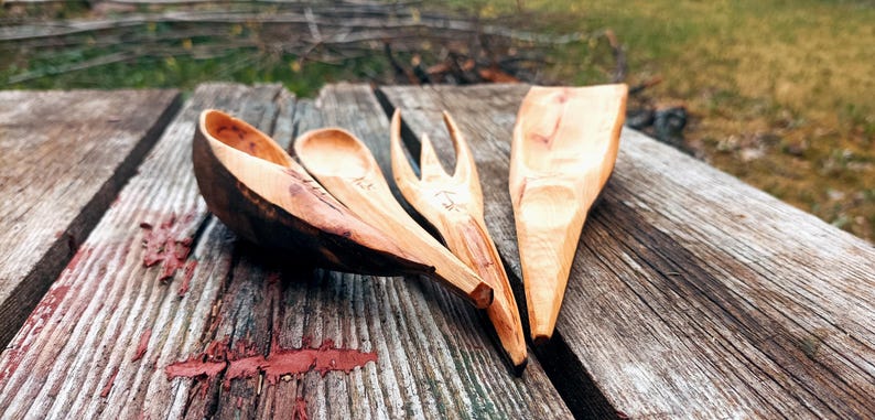 K&ouml;nnte beinhalten: Ein Set aus vier handgeschnitzten K&uuml;chenutensilien aus Holz: ein gro&szlig;er L&ouml;ffel, ein kleiner L&ouml;ffel, eine Gabel und ein Spatel. Die Utensilien sind aus hellem Holz mit dunkelbraunen Akzenten gefertigt.