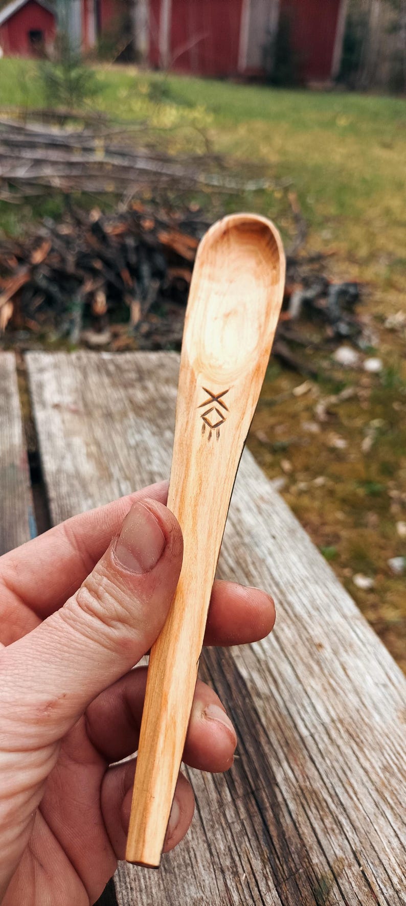 K&ouml;nnte beinhalten: Handgeschnitzter Holzl&ouml;ffel mit hellbraunem Finish. Der L&ouml;ffel hat ein geschnitztes Design in der N&auml;he des Griffs. Der unscharfe Hintergrund deutet auf ein rustikales oder nat&uuml;rliches Thema hin.