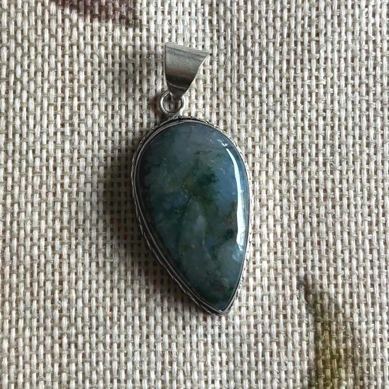 Peut inclure: Un pendentif en argent avec une pierre d'agate verte et grise. La pierre est en forme de larme et pr&eacute;sente un motif naturel et organique.