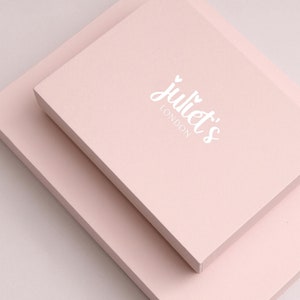May include: Two pale pink boxes stacked on top of each other. The top box has the text "juliet's LONDON" printed in white.