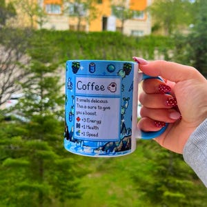 Könnte beinhalten: Eine blau-weiße Kaffeetasse mit blauem Henkel. Auf der Tasse steht das Wort "Coffee" und der Text "It smells delicious. This is sure to give you a boost. +3 Energy, +1 Health, +1 Speed."