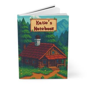 Puede incluir: Un cuaderno de tapa dura con una ilustración pixelada de una cabaña en un bosque. La portada muestra el texto "Katie's Notebook" en un diseño de letrero de madera, sobre un fondo de árboles y montañas.