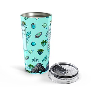Puede incluir: Un vaso de viaje turquesa con borde plateado y tapa transparente. El vaso est&aacute; decorado con gr&aacute;ficos pixelados de varios objetos y texto. El texto del vaso es parcialmente visible. La tapa est&aacute; a un lado.