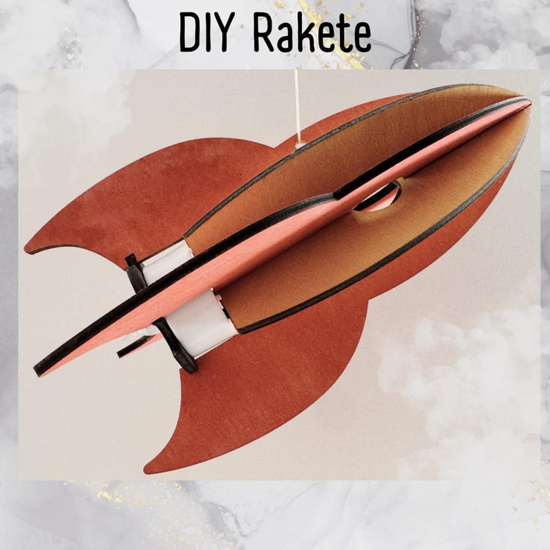 Może przedstawiać: DIY Rakete, rakieta z drewna w kolorze czerwonym i brązowym z czarnymi ozdobami. Rakieta jest zawieszona na sznurku.