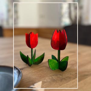 Può includere: Due tulipani di legno dipinti di rosso e verde. I tulipani sono su un tavolo di legno.