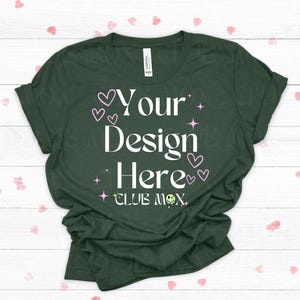 May include: Dark green t-shirt with the text "Your Design Here" in white, accented with pink hearts and stars. The shirt also features the text "CLUB MOX" with a small smiley face. A casual tee for custom designs.