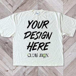 May include: A white t-shirt with black text that says "YOUR DESIGN HERE" and "CLUB MOX" with a smiley face graphic.