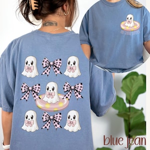 May include: Blue jean colored t-shirt featuring a ghost graphic with a pink bow and a pink and black checkered bow. The shirt also has the text "HOT GHOUL SUMMER" and the word "blue jean".