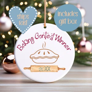 May include: White ceramic Christmas ornament with a pie graphic and the text "Baking Contest Winner." A rolling pin graphic and the year "20XX" are below the pie. Includes a heart-shaped tag that says "ships fast" and a round tag that says "includes gift box."