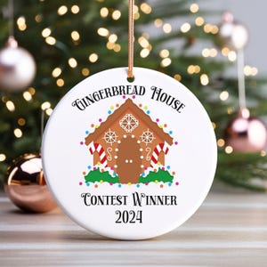 May include: White round Christmas ornament with a gingerbread house design. The ornament features a brown gingerbread house with colorful candy lights, red and white striped candy canes, and the text "Gingerbread House Contest Winner 2024".