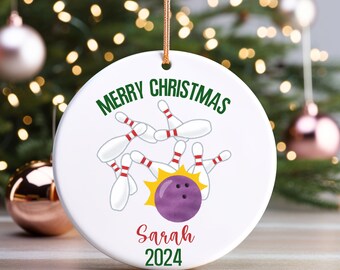 May include: White ceramic Christmas ornament with a bowling ball and pins design. The text "Merry Christmas" is written in green letters. The name "Sarah" and the year "2024" are written in red letters.