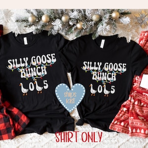 May include: Two black t-shirts with the text "SILLY GOOSE BUNCH LOL 5" in white, with a string of colorful lights and goose illustrations. The shirts are displayed on a white surface with holiday decorations.