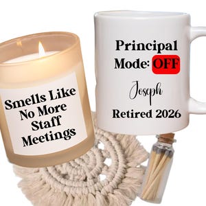 May include: A lit candle in a glass jar with the text "Smells Like No More Staff Meetings" and a white mug with "Principal Mode: OFF" and "Retired 2026" printed on it. A small glass vial of matches is next to the mug.