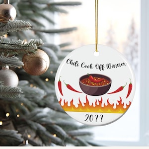 May include: A white ceramic Christmas ornament with a gold string. The ornament features the text "Chili Cook Off Winner" above a bowl of chili and chili peppers. Flames and the number "20??" are at the bottom.