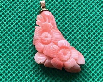 May include: A light pink carved pendant featuring two layered floral blossoms with detailed petals. The pendant is attached to a small gold-toned metal bail at the top, designed for suspension on a necklace chain or cord.