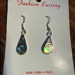 Op de afbeelding: Een paar druppelvormige oorbellen met iriserende abalone schelpinzetstukken, gezet in zilverkleurig metaal. De oorbellen worden gepresenteerd op een witte kaart met de tekst "Fashion Earring" en "NEW YORK &bull; PARIS".