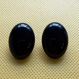 Puede incluir: Un par de pendientes ovalados negros. Los pendientes están hechos de un material liso y brillante.