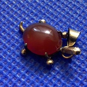 May include: A gold-toned pendant featuring a red carnelian gemstone set in a turtle design. The pendant has a loop for attaching to a chain.