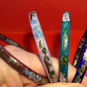 Op de afbeelding: Vier emaille armbanden met bloemmotieven. De armbanden zijn in tinten paars, blauw, groen en rood.