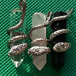 May include: Three crystal pendants wrapped in silver snake designs. The crystals are clear, white, and black.