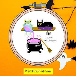 May include: A cross-stitch design in a round frame featuring a Halloween theme. The design includes a frog pouring pink liquid into a cauldron, a black cat, and the words "Happy Halloween". The background is orange.
