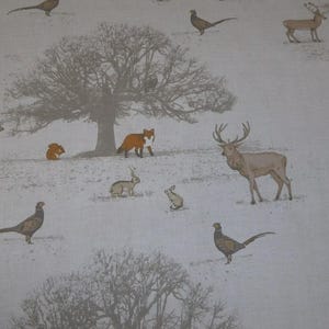 May include: A textile featuring a woodland scene with deer, pheasants, foxes, and rabbits. The design uses a muted colour palette of beige, brown, and orange. A large tree is centrally positioned.