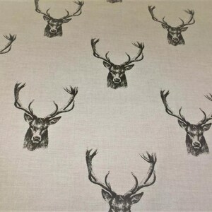 May include: A pale fabric with a repeating pattern of black deer heads, each with prominent antlers. The deer heads are shaded to give a textured look. The design has a rustic, nature-inspired theme, suitable for home decor or textiles.