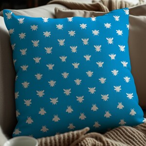 Peut inclure: Un coussin bleu avec un motif d'abeilles blanches. Le coussin est posé sur un canapé brun.