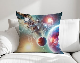 May include: A throw pillow with a colourful galaxy print featuring two astronauts in white outline. The background is a mix of blue, purple, pink and orange hues with stars and planets.