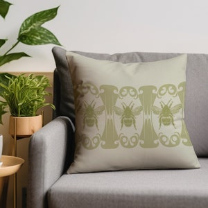 May include: A beige throw pillow with a decorative border of stylized bees and floral motifs in a muted green color.