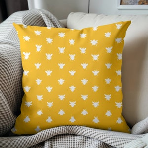 May include: A yellow cushion with a white bee pattern. The cushion is on a sofa with a grey and white throw.