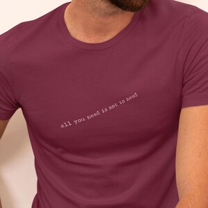 May include: A maroon t-shirt with the text "all you need is not to need" printed in white on the front.