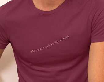 May include: A maroon t-shirt with the text "all you need is not to need" printed in white on the front.