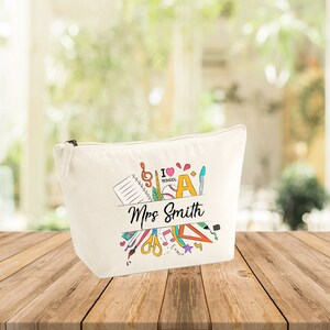 Puede incluir: Una bolsa de lona blanca con cremallera con un diseño colorido de útiles escolares y el texto "Mrs. Smith".