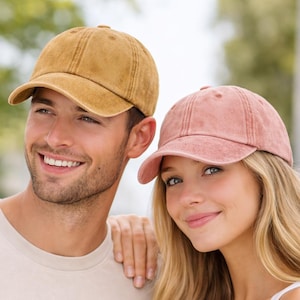 May include: Two baseball caps, one in mustard yellow and the other in dusty rose. Both caps have a curved peak and a classic six-panel design. The caps are made of a soft, textured material.