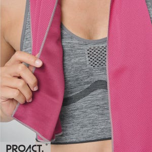 Op de afbeelding: Een roze sportdoek met een mesh textuur is over een grijze sportbeha gedrapeerd. De handdoek heeft een grijze rand en de merknaam "PROACT." is linksonder zichtbaar. De sportbeha heeft een gestructureerd patroon.