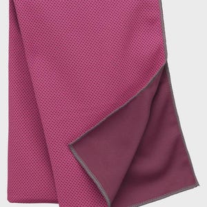 Op de afbeelding: Een opgevouwen magenta koelhanddoek met een getextureerd, gestippeld oppervlak. De onderkant van de handdoek is effen donkerder magenta, met een grijze gestikte rand. De handdoek is ontworpen om te koelen en wordt waarschijnlijk gebruikt voor sport of buitenactiviteiten.