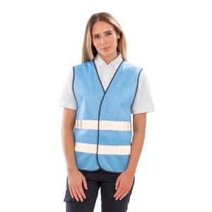 Op de afbeelding: Een lichtblauw veiligheidsvest met twee reflecterende witte banden. Het vest heeft een V-hals en een ritssluiting.