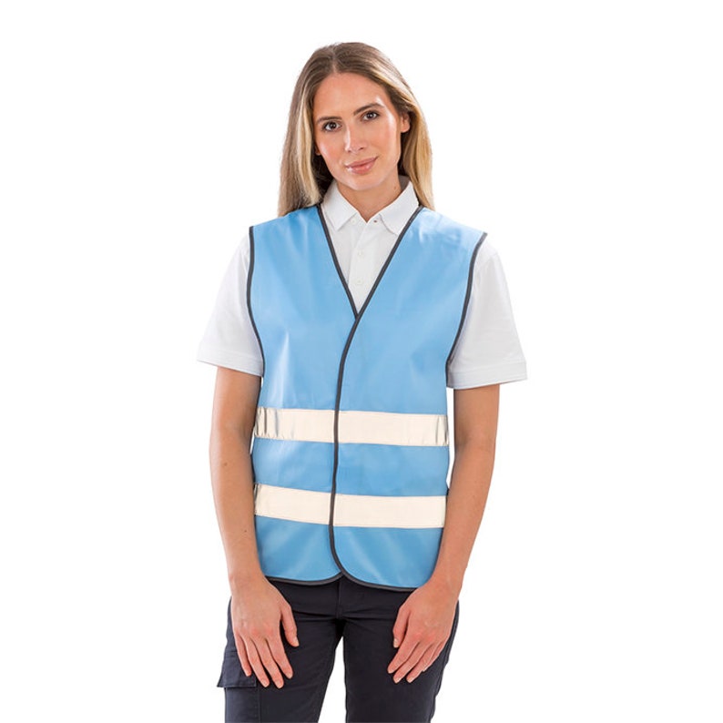 Op de afbeelding: Een lichtblauw veiligheidsvest met twee reflecterende witte banden. Het vest heeft een V-hals en een ritssluiting.