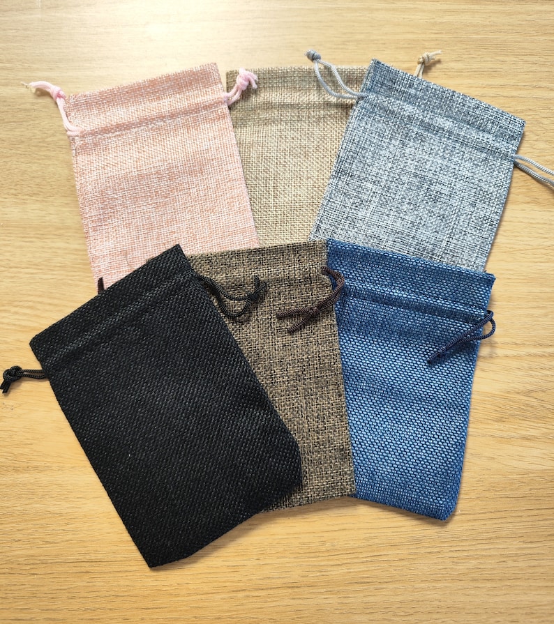 Puede incluir: Seis peque&ntilde;as bolsas de cord&oacute;n de tela de arpillera en varios colores, incluyendo rosa, beige, gris, negro, marr&oacute;n y azul.
