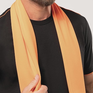 Op de afbeelding: Een oranje koelhanddoek gedrapeerd om de nek van een persoon. De handdoek heeft een gestructureerd oppervlak en wordt gecombineerd met een zwart t-shirt met oranje afwerking. De handdoek is gemaakt van lichtgewicht, ademend materiaal.