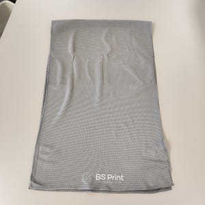 Op de afbeelding: Een grijze, rechthoekige koelhanddoek met een geperforeerde textuur. De handdoek is opgevouwen en ligt plat op een wit oppervlak. De tekst "BS Print" is in het wit gedrukt in de rechter benedenhoek.