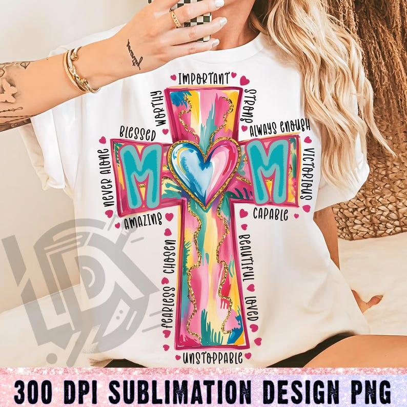 May include: A white t-shirt with a colorful cross design featuring the word "MOM" and positive affirmations like "worthy", "blessed", "amazing", "capable", "unstoppable", "fearless", "chosen", "beautiful", "loved", "important", "strong", "always enough", "never alone", "victorious".