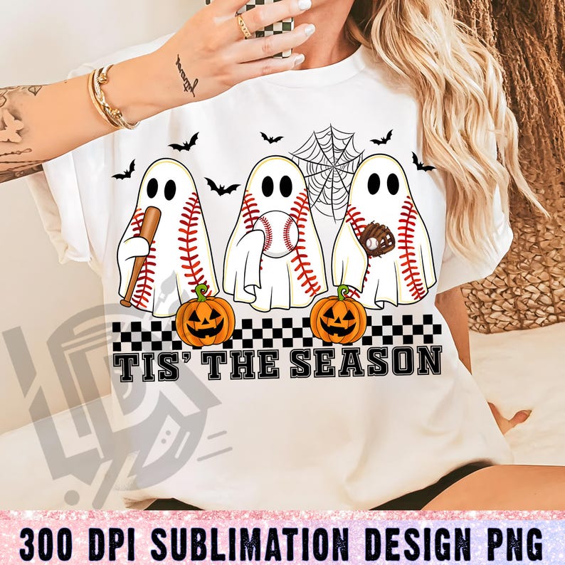 May include: White t-shirt featuring a Halloween-themed design. The graphic includes three ghost figures with baseball stitching, bats, baseballs, and gloves. The phrase "Tis' The Season" is printed below the ghosts, with jack-o'-lanterns and bats.