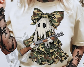May include: Cream-colored t-shirt featuring a cartoon ghost in camouflage attire, holding a shotgun. The ghost has a large bow and a ruffled skirt, both in a camouflage pattern. The text "300 DPI SUBLIMATION DESIGN PNG" is at the bottom.