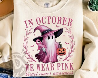May include: Cream-colored sweatshirt with a pink ghost wearing a witch hat and holding a pink ribbon and a jack-o'-lantern. The text reads "IN OCTOBER WE WEAR PINK breast cancer awareness".