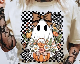 May include: Cream-colored t-shirt featuring a ghost design with a brown bow, holding a pumpkin basket filled with flowers. The ghost is set against a black and white checkered background with bats and stars. The text "300 DPI SUBLIMATION DESIGN PNG" is at the bottom.